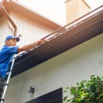 Homeowner cleaning the gutters of his home. Spring cleaning his home roof.